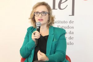 Photo of Roberta Rronka, a fair skin blonde woman in a blue jacket speaking on a microphone.