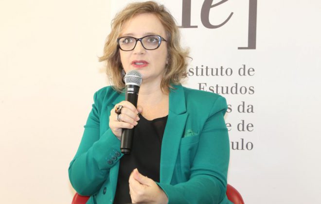 Photo of Roberta Rronka, a fair skin blonde woman in a blue jacket speaking on a microphone.