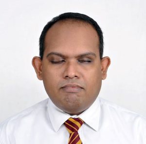 A dark-haired man in a white shirt anda re-and-yellow striped tie