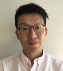 A photo of a dark haired man with a short haircut wearing glasses in a light shirt.